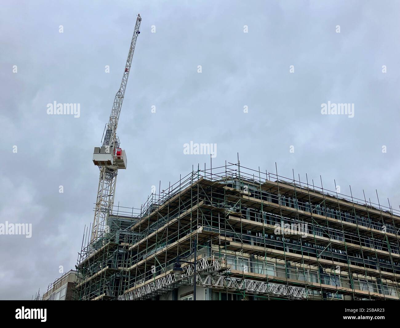 Großer Kran, der an einem Gebäude mit Gerüsten arbeitet - Smartphone-aufgenommenes Stockfoto