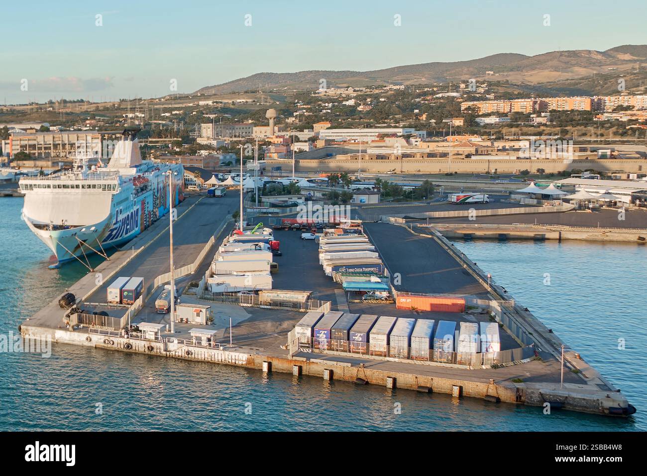 Civitavecchia, Italien - 2. Februar 2025: Lkw, Container und eine Fähre in einem belebten italienischen Hafen, in dem Logistik, Handel und Transportnetz in den Vordergrund gestellt werden Stockfoto