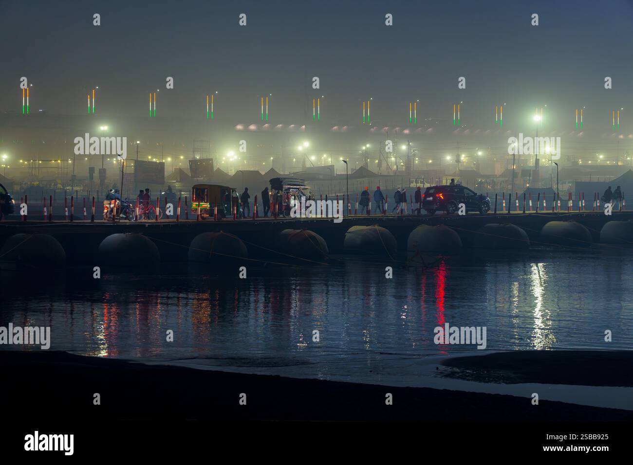Prayagraj, Uttar Pradesh, Indien, 11. Januar 2025. Nebelige Nacht auf der Mahakumbh Mela Pontonbrücke mit Pilgern, die unter Laternen überqueren. Stockfoto