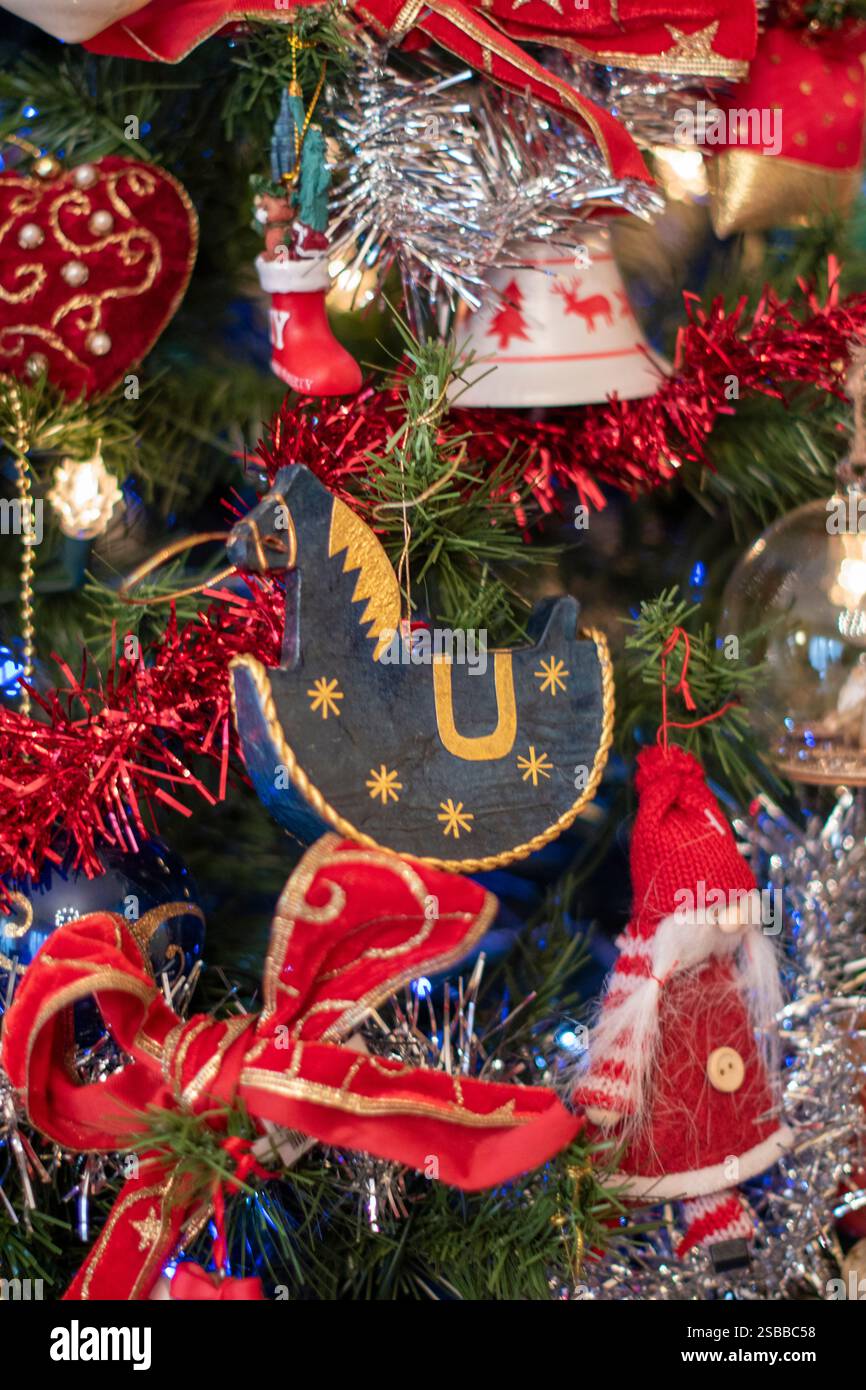 Ein Schaukelpferd, das einen weihnachtsbaum mit Kugeln, Flocken und Elfen dekoriert. Stockfoto