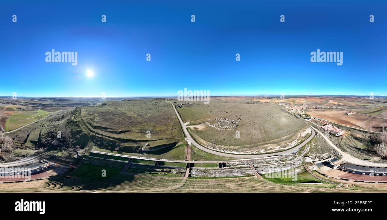 Blick aus der Vogelperspektive auf ein altes römisches Amphitheater von Clunia mit Steinen und einem grasbewachsenen Bühnenbereich. Das kreisförmige Layout ist sichtbar und zeigt die Zeilen Stockfoto
