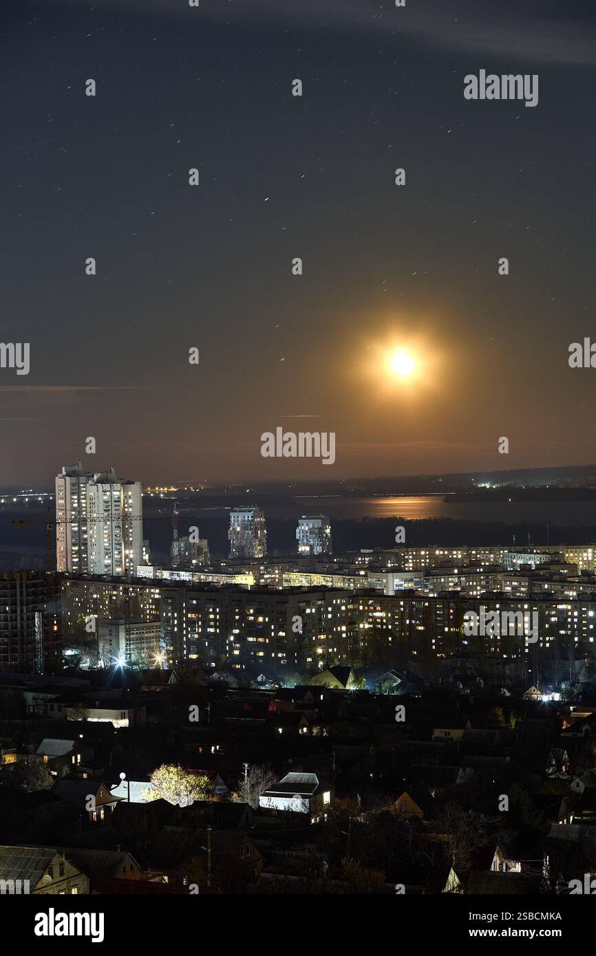 Heller Mond erstrahlt in der Stadtlandschaft, Flusstreflexion in der urbanen Szene, Sternenhimmel, abendliche Atmosphäre, Stadtlichter, himmlisches Stimmungskonzept Stockfoto