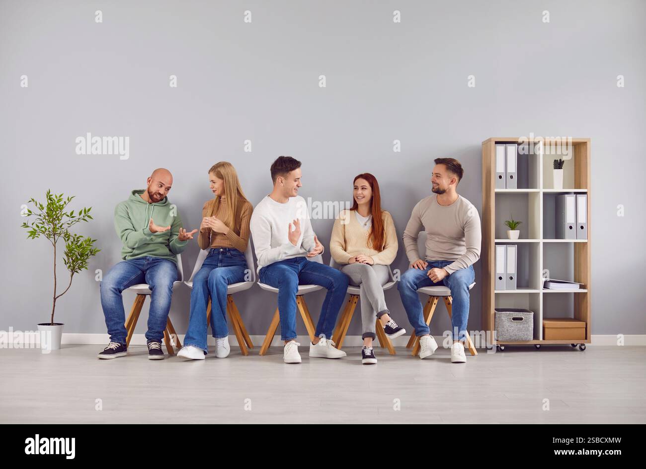 Junge Menschen in lässiger Kleidung sitzen auf Stühlen in der Reihe und warten auf die Umkehr der Intervieweinladung Stockfoto