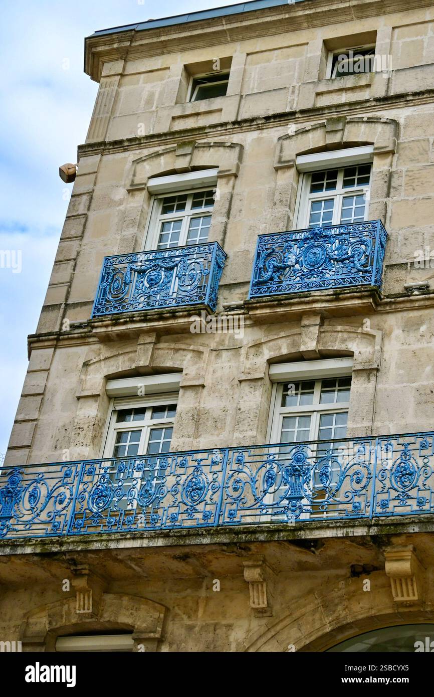 Eine Nahaufnahme eines historischen französischen Gebäudes mit blauen schmiedeeisernen Balkonen, cremefarbenen Wänden und traditionellen Fenstern unter einem weichen, bewölkten Himmel. Stockfoto
