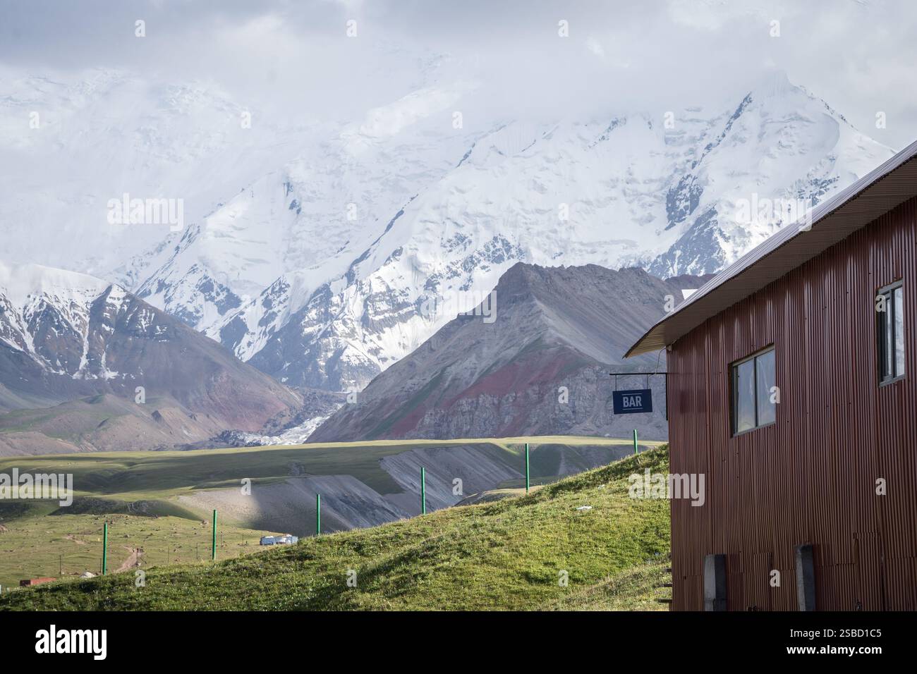 Gebäude mit Bar-Schild im Expeditionscamp mit riesigen verschneiten Pamir-Bergen im Hintergrund, Kirgisistan Stockfoto