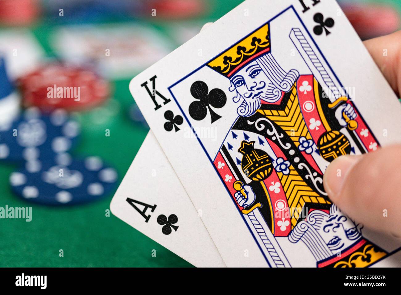 Eine Nahaufnahme eines Pokerspielers mit einem Ass und einem König von Clubs, auch bekannt als „Ace-King“ oder „Big Slick“. Der grüne Filztisch, Pokerchips Stockfoto