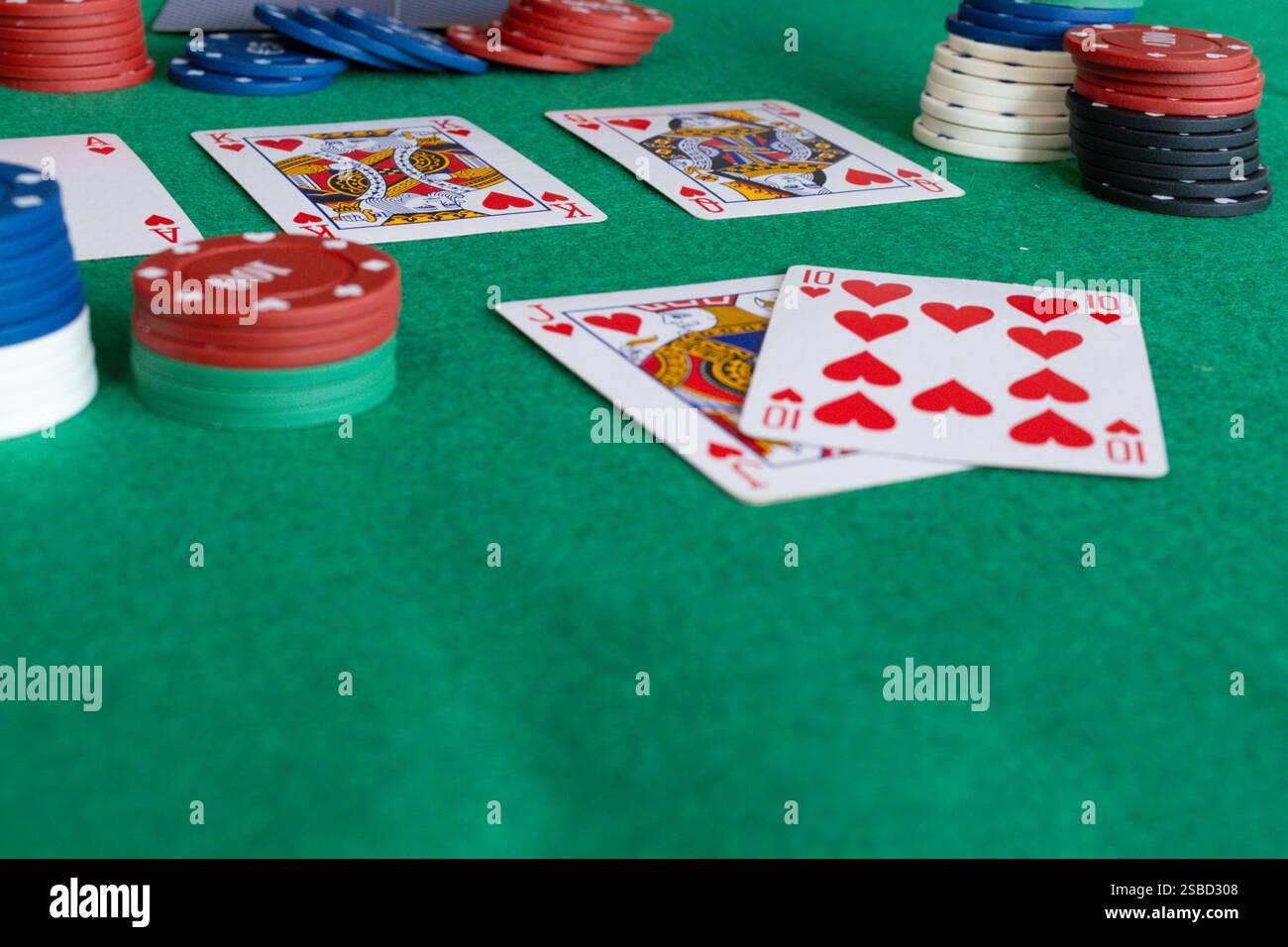 Pokerspiel läuft mit einer Nahaufnahme der Karten und Stapel von Pokerchips auf einem grün matten Tisch. Die abgebildeten Karten enthalten eine zehn und einen Herzklopfen, Stockfoto