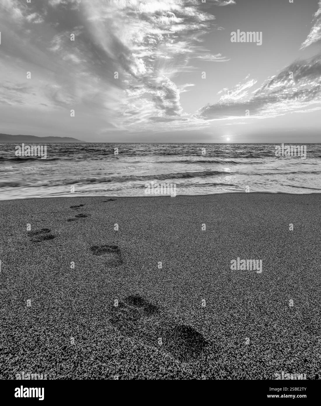 Fußspuren im Sand, die in Richtung Ocean Sunrise Black and White vertikal führen Stockfoto