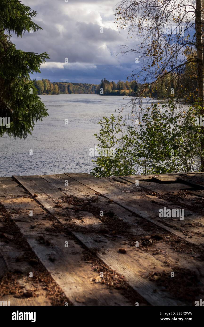 Ein ruhiger Moment am Fluss – Reflektionen im Wald, eine Holzterrasse und vergessene Kochutensilien, die auf eine Geschichte hinweisen, die in der Umarmung der Natur zurückgeblieben ist Stockfoto