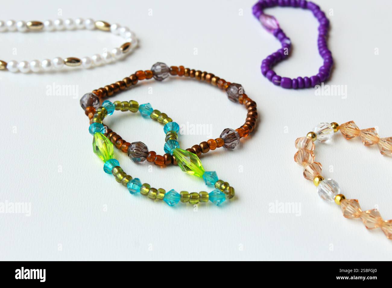 Armbänder mit Perlen und braunen, grünen und violetten Perlen. Stilvolle trendige Modeaccessoires, Modeschmuck, handgefertigte Bijouterie auf weißem Hintergrund. Stockfoto