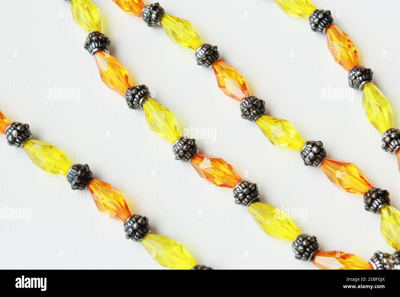 Elegante gelbe und orangefarbene Perlen mit metallischen Abstandshaltern auf weißem Hintergrund. Stilvolles Zubehör für die Schmuckherstellung, ideal für Modeaccessoires. Stockfoto