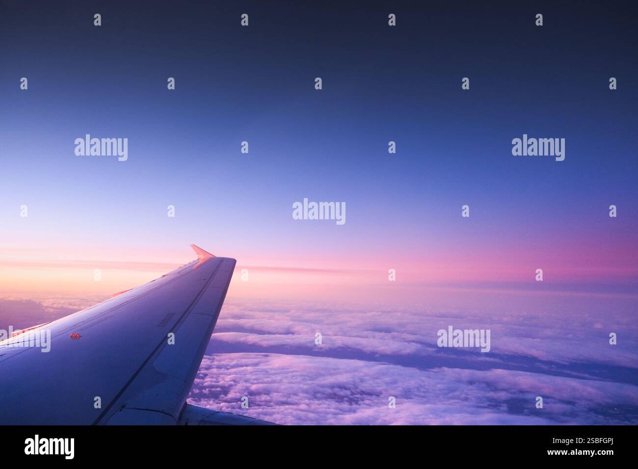 Der Flügel eines Privatjets fliegt über einem bewölkten Himmel bei Sonnenuntergang über Spanien. Der Blick vom Fenster des Flugzeugs ist magisch und die Farben des Himmels sind es Stockfoto