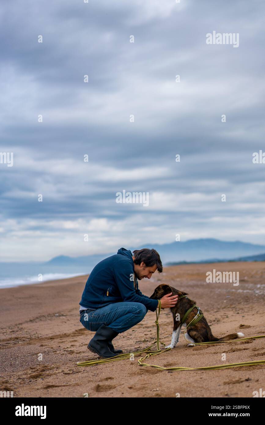 Mann, der emotional auf seinen Hund am Sandstrand blickt Stockfoto