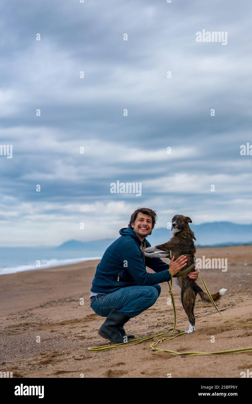 Mann mit Hund, der an einem Sandstrand zur Kamera schaut Stockfoto