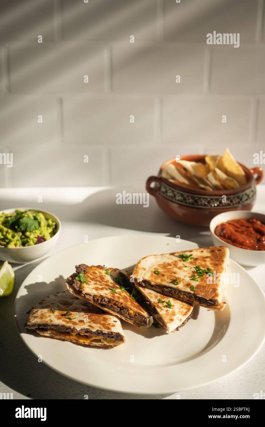 Quesadillas aus schwarzen Bohnen mit Guac, Salsa und Chips auf der Küchenzeile Stockfoto