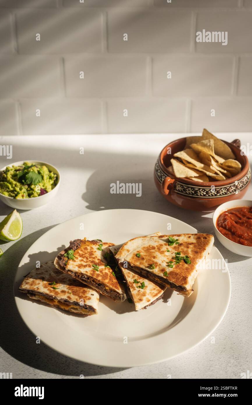 Vegane Quesadillas aus schwarzen Bohnen mit Guacamole, Salsa und Tortillachips Stockfoto