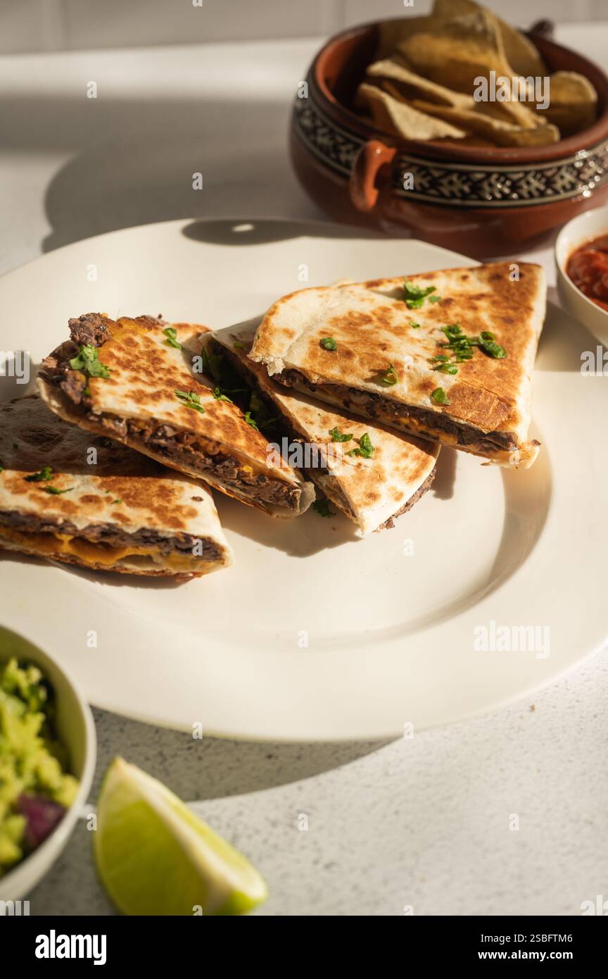 Vegane Quesadillas aus schwarzen Bohnen mit Guacamole, Salsa und Chips auf weiß Stockfoto