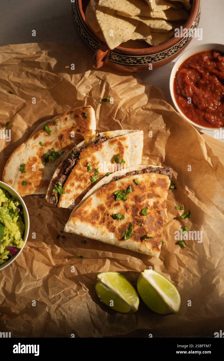 Vegetarische Schwarzbohnen-Quesadillas auf Pergamentpapier mit Beilagen Stockfoto