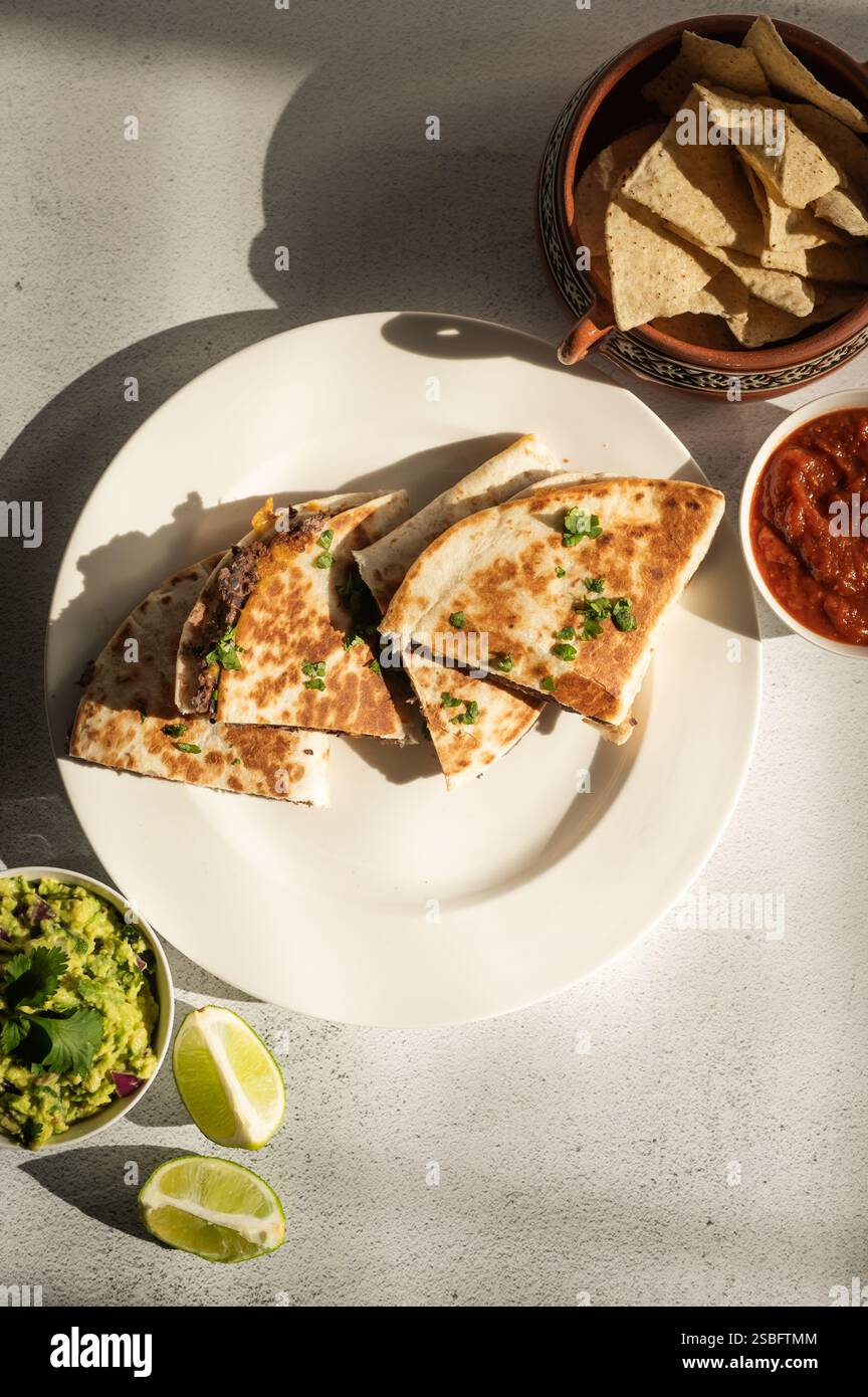 Knusprige Quesadillas aus schwarzen Bohnen mit Guac, Salsa und Tortillachips Stockfoto