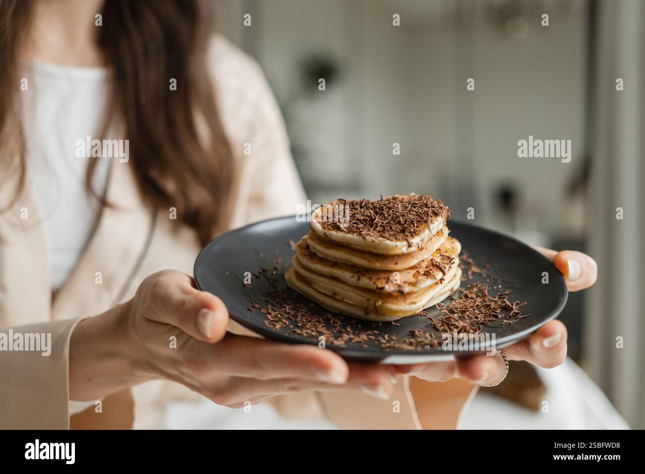 Frau, die Teller mit herzförmigen Pfannkuchen mit geriebener Schokolade hält Stockfoto