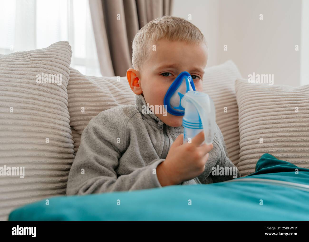 Kranker Junge, der zu Hause auf Sofa Inhalator sitzt medizinische Ausrüstung Atemmaske. Hochwertige Fotos Stockfoto