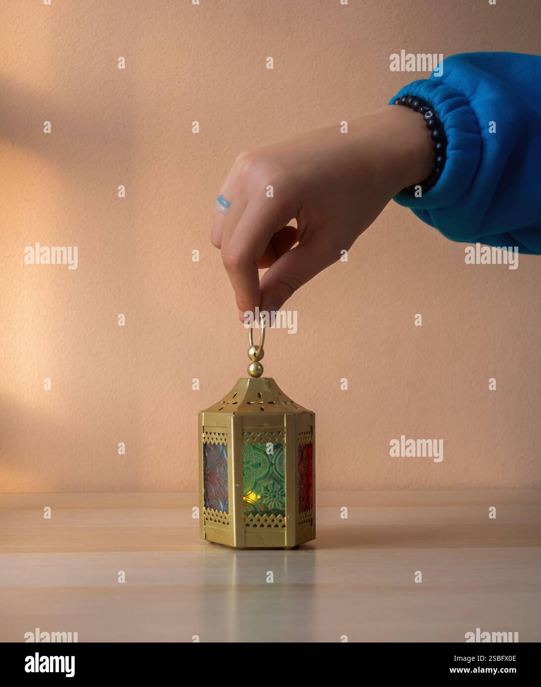 Menschliche Hand, die Eine Ramadan-Laterne mit bunten Glaspaneelen hält Stockfoto