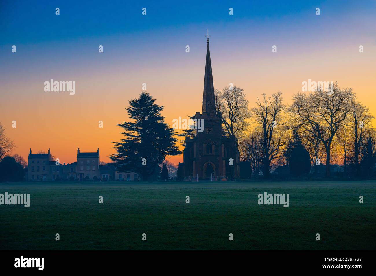 Ein nebeliges Dorf grün bei Sonnenaufgang mit der Silhouette einer Kirche Stockfoto