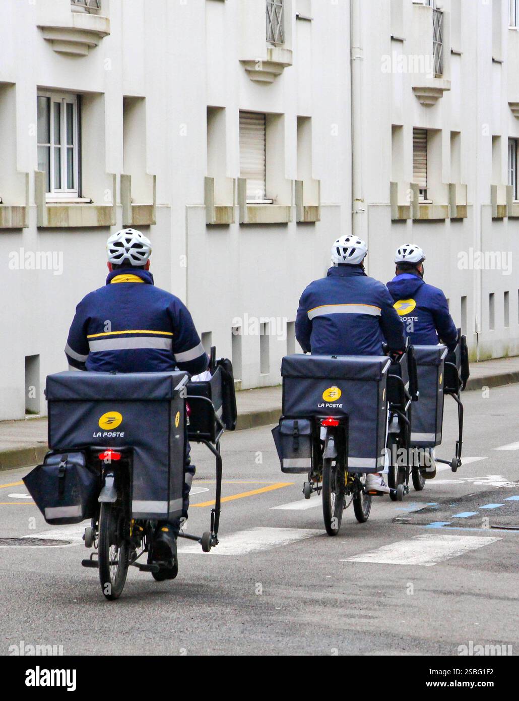 Vannes (Bretagne, Nordwestfrankreich): Drei Postboten aus La Poste auf Fahrrädern, von hinten gesehen, begeben sich auf eine Postzustellungsrunde. Stockfoto