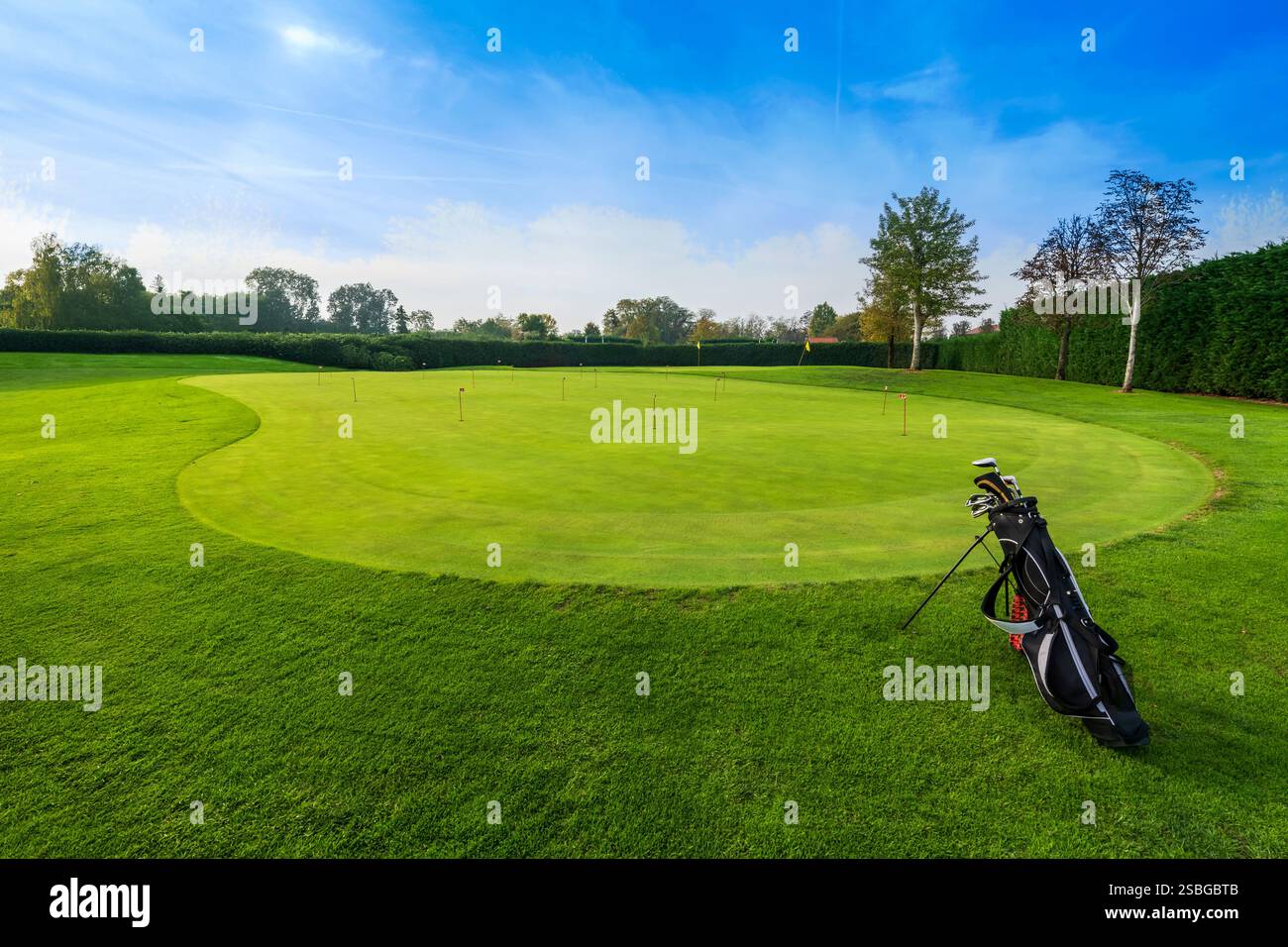 Golftasche mit mehreren Schlägern, die auf einem perfekt gemähten Putting Green in einem Golfplatz stehen, bereit für Golfer zum Üben Stockfoto