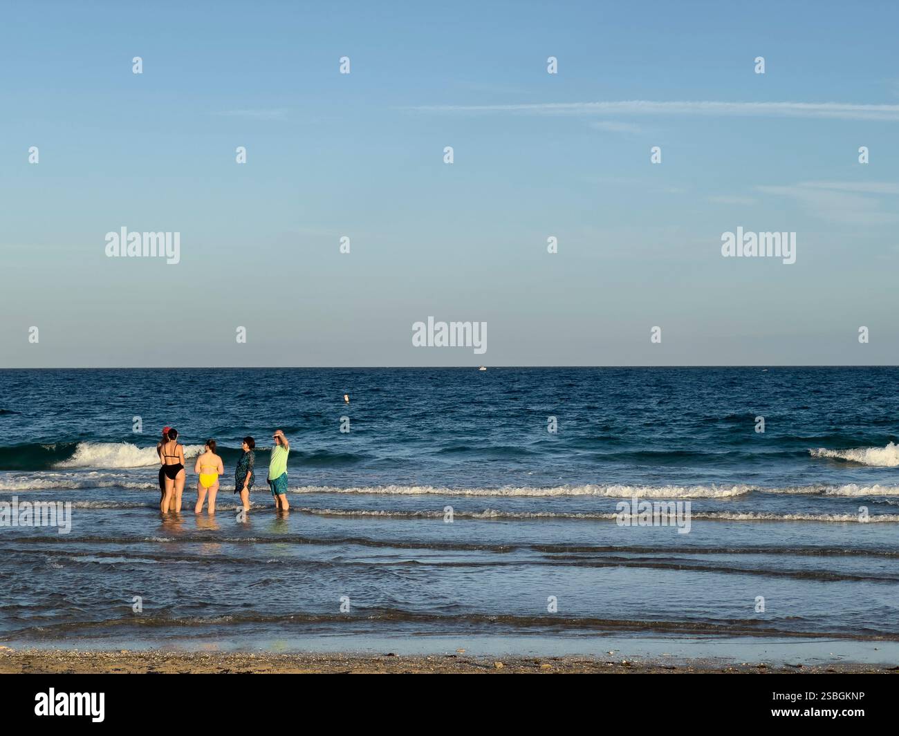 Eine Gruppe von Strandgängern steht im flachen Wasser von Lauderdale am Sea Beach und blickt unter dem warmen Nachmittagslicht auf das Meer - Smartphone-aufgenommenes Stockfoto