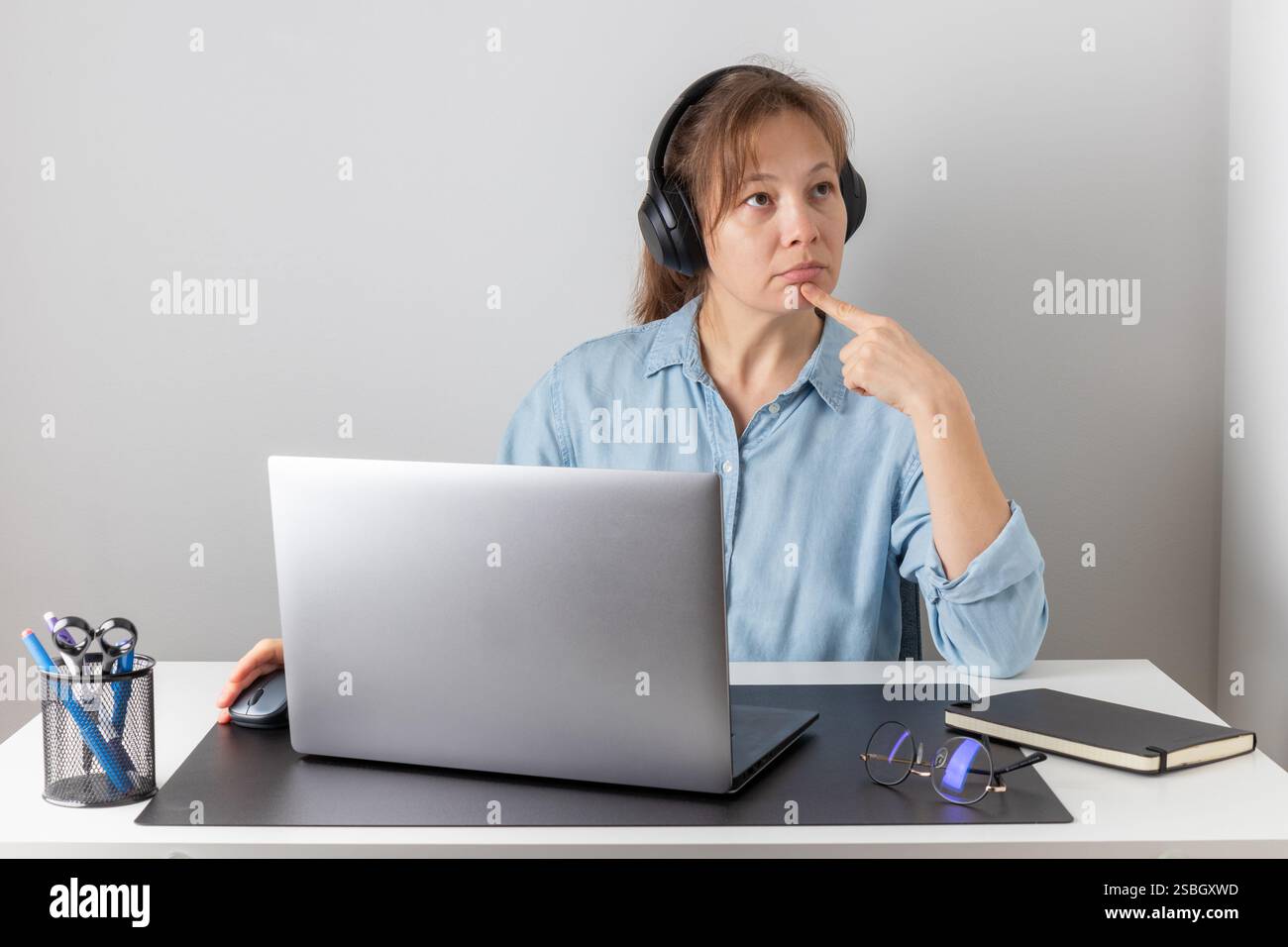 Eine Frau denkt darüber nach, während sie einen Laptop verwendet, denkt, online studiert oder ein virtuelles Telefongespräch von zu Hause aus erledigt, denkt über die Antwort nach Stockfoto