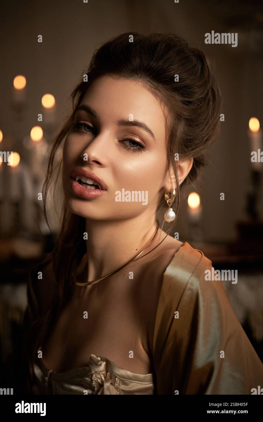 Eine junge Frau mit ätherischer Schönheit verkörpert einen mystischen Vampir, umgeben von flackernden Kerzen. Stockfoto