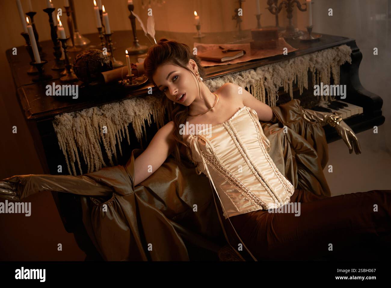 Eine junge Frau in gotischer Mode loungt an einem Flügel und strahlt Rätsel aus. Stockfoto