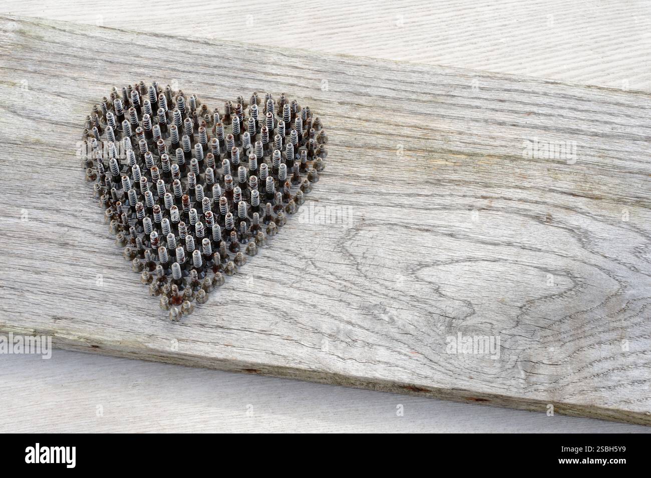 Herzform aus kleinen Holzbearbeitungsschrauben aus Metall, die auf dem Kopf stehen und Schulter an Schulter stehen. Hintergrund des verwitterten Holzes. Stockfoto