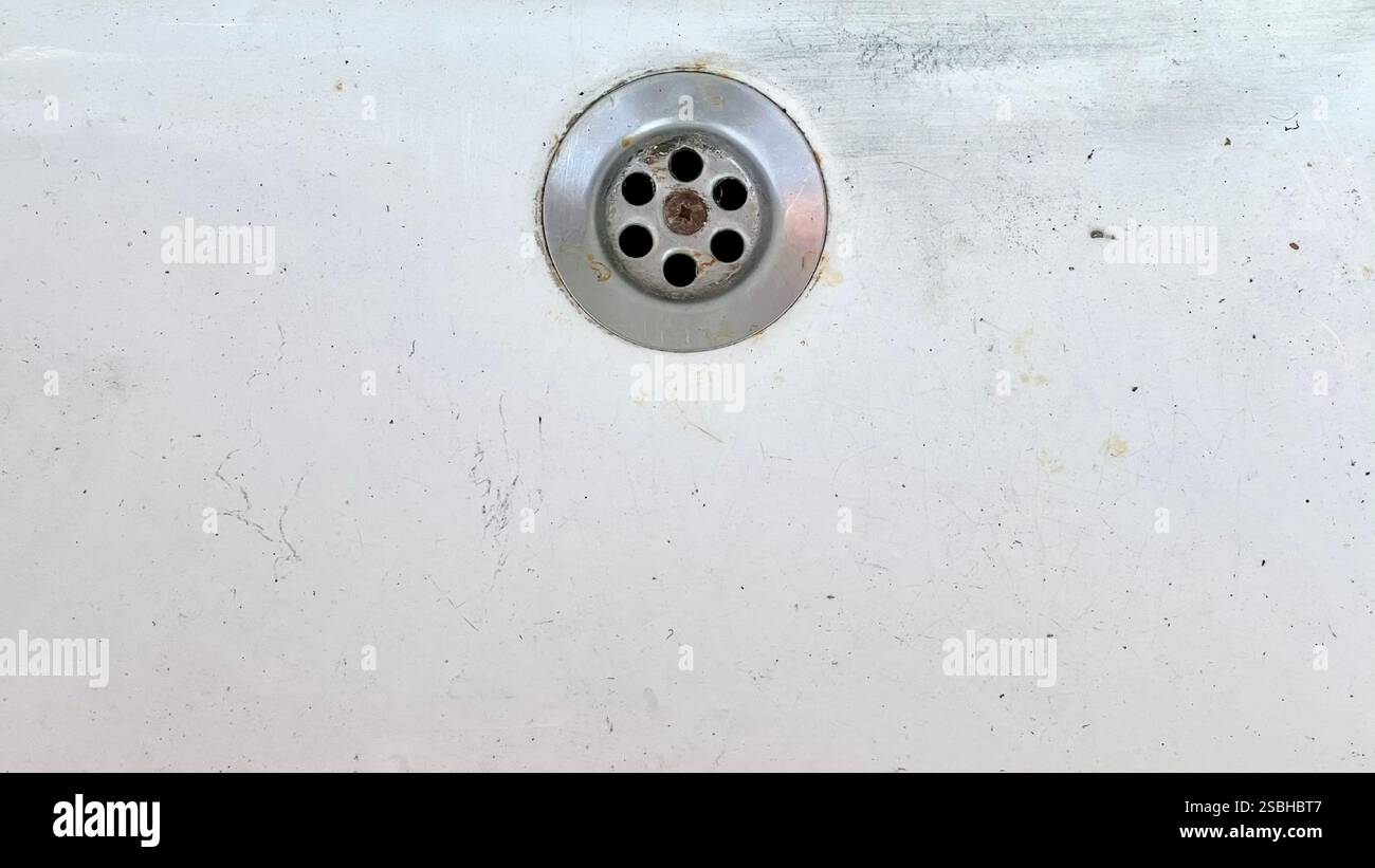 Ein kleiner runder Ablauf auf einer abgenutzten weißen Oberfläche, der Schmutz und Alter durch den Gebrauch zeigt. Stockfoto