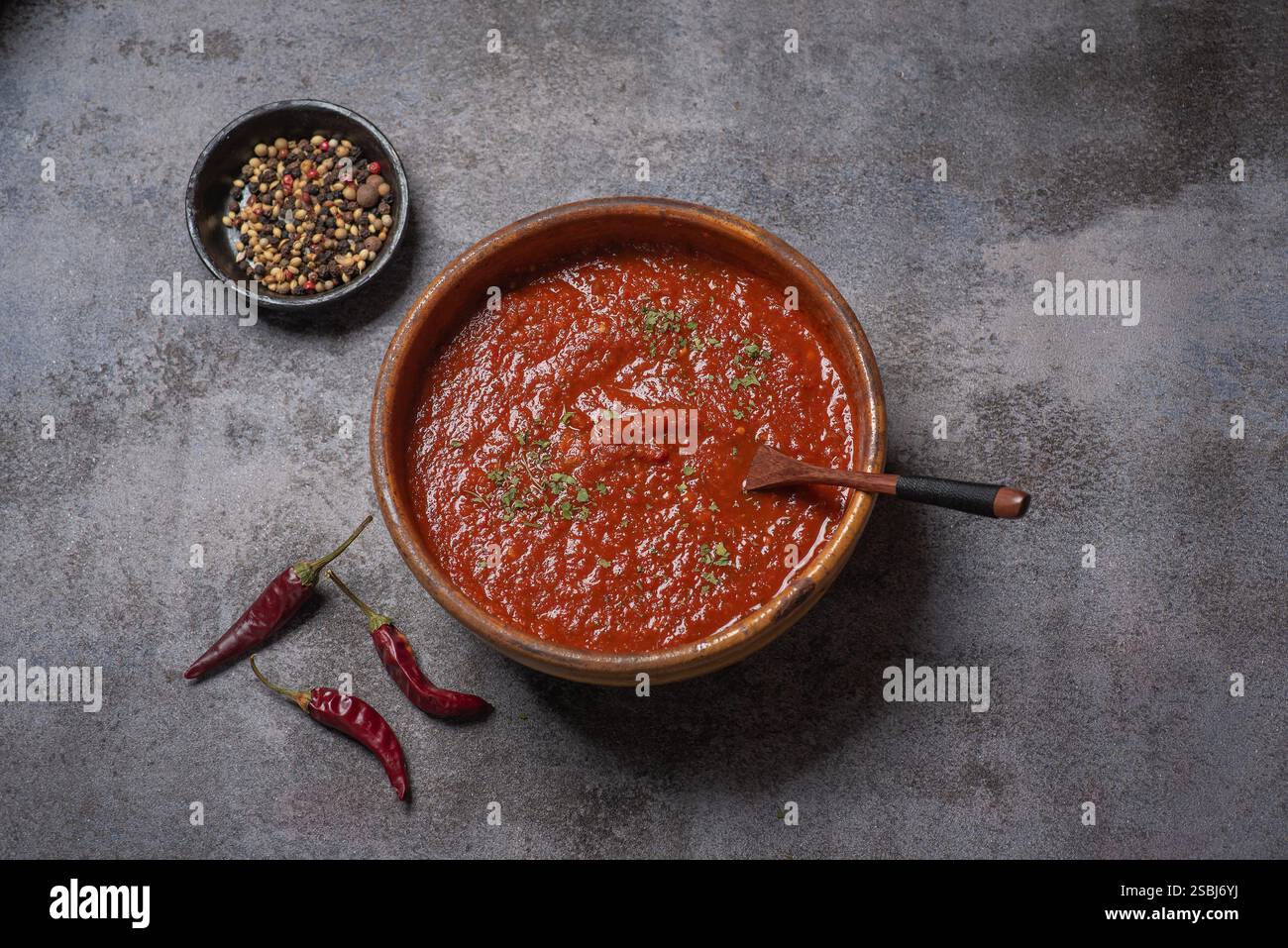 Eine tiefrote Sauce in einer traditionellen Tonschale, garniert mit Kräutern, verkörpert die Wärme hausgemachter Gerichte und ist eine ideale Basis für verschiedene Gerichte. Stockfoto Eine tiefrote Sauce in einer traditionellen Tonschale, garniert mit Kräutern, verkörpert die Wärme hausgemachter Gerichte und ist eine ideale Basis für verschiedene Gerichte. Stockfoto