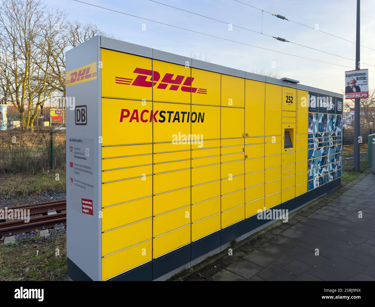 Bocholt, Deutschland, Europa, DHL Packstation, Smart City, Digitalisierung, Logistik, Onlinehandel, E-Commerce, nachhaltige Lieferketten, Paketdienstleister, COâ-Reduktion, Klimaschutzmaßnahmen, urbane Infrastruktur, Fachkräftemangel, Automatisierung, kontaktlose Lieferung, Bahnlogistik, Verkehrswende, Deutsche Bahn, steigende Lebenshaltungskosten, Konsumverhalten, Inflation, soziale Gerechtigkeit, Einzelhandel, Wettbewerbsdruck, Kapitalismuskritik, politische Plakate, EU-Handelspolitik. *** Bocholt, Deutschland, Europa, DHL Packstation, Smart City, Digitalisierung, Logistik, Online-Handel, E-Comme Stockfoto