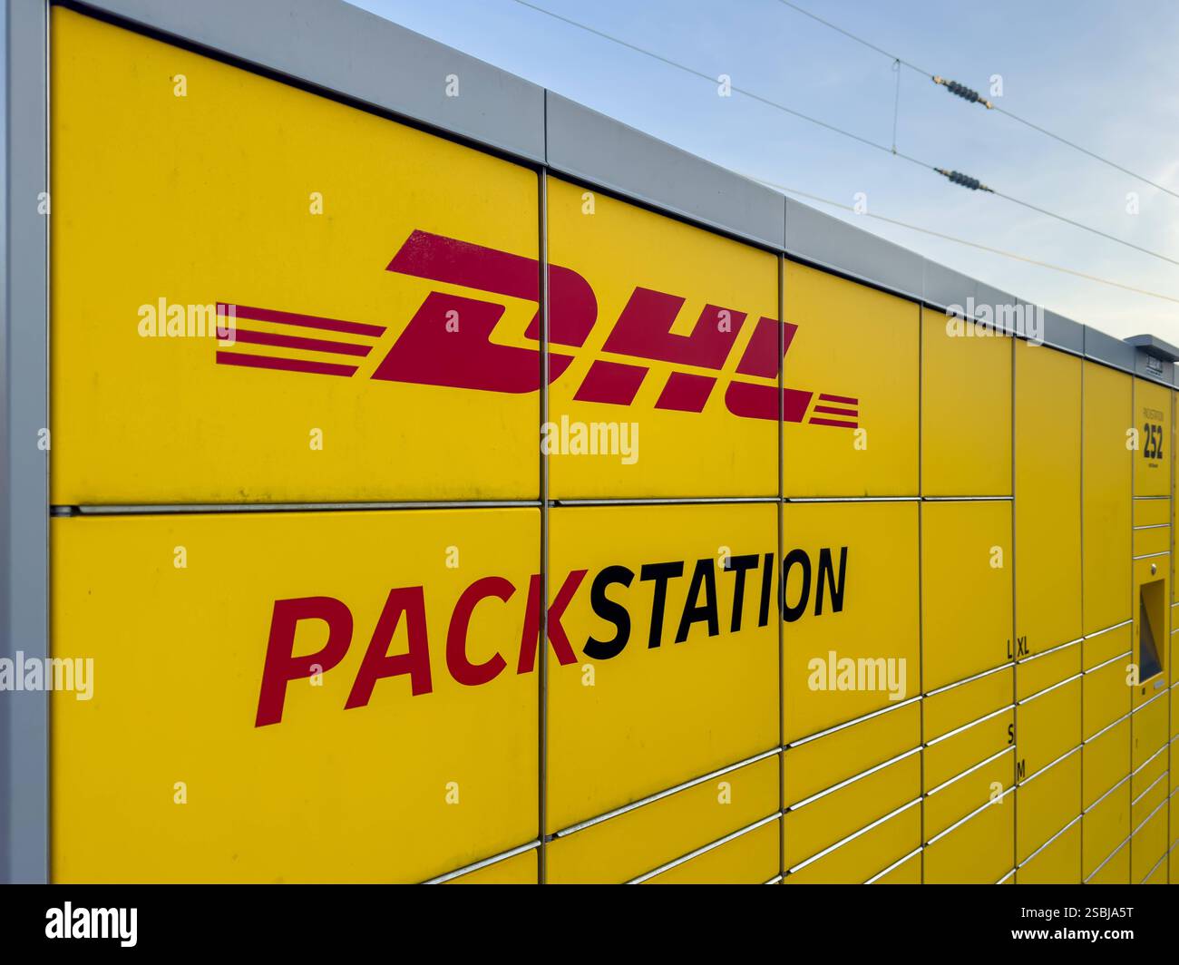 Bocholt, Deutschland, Europa, DHL Packstation, Smart City, Digitalisierung, Logistik, Onlinehandel, E-Commerce, nachhaltige Lieferketten, Paketdienstleister, COâ-Reduktion, Klimaschutzmaßnahmen, urbane Infrastruktur, Fachkräftemangel, Automatisierung, kontaktlose Lieferung, Bahnlogistik, Verkehrswende, Deutsche Bahn, steigende Lebenshaltungskosten, Konsumverhalten, Inflation, soziale Gerechtigkeit, Einzelhandel, Wettbewerbsdruck, Kapitalismuskritik, politische Plakate, EU-Handelspolitik. *** Bocholt, Deutschland, Europa, DHL Packstation, Smart City, Digitalisierung, Logistik, Online-Handel, E-Comme Stockfoto