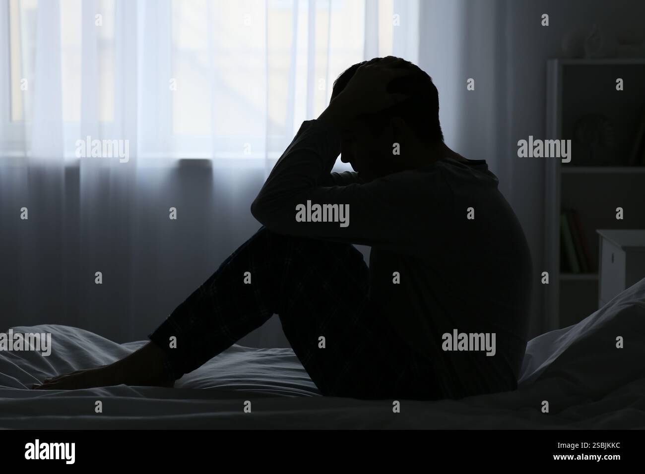 Silhouette eines depressiven jungen Mannes, der in einem dunklen Schlafzimmer sitzt Stockfoto