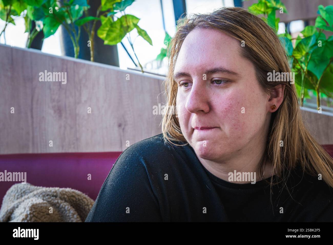 Eine Frau sitzt nachdenklich, verloren in ihren Reflexionen, während Grün um sie herum in einer einladenden Café-Atmosphäre gedeiht. Stockfoto