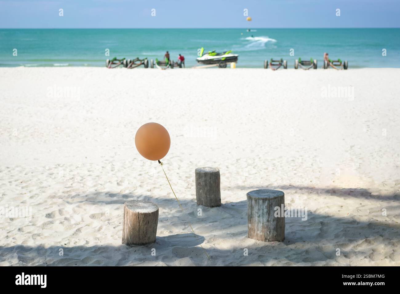 Strandszene mit Ballon und Holzhocker, mit verschwommenem Hintergrund von Wassersportaktivitäten. Sommer-Konzept. Stockfoto