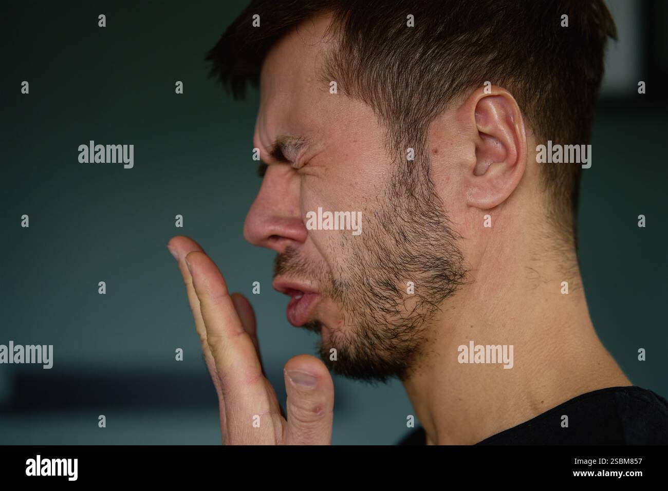 Schlechter Atem aus dem Mund. Nahaufnahme eines Mannes, der seinen Atem überprüft, indem er in seine Hand ausatmet, und zeigt Bedenken über Mundhygiene oder schlechten Atem Stockfoto