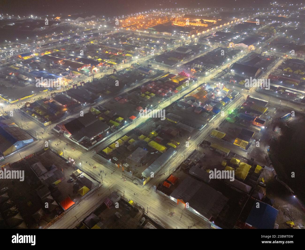 Drohnenblick auf die Zeltstadt Mahakumbh bei Nacht, mit vereinzeltem Nebel und glühenden Zelten. Eine atemberaubende Szene voller Hingabe, die die Weite zeigt. Stockfoto