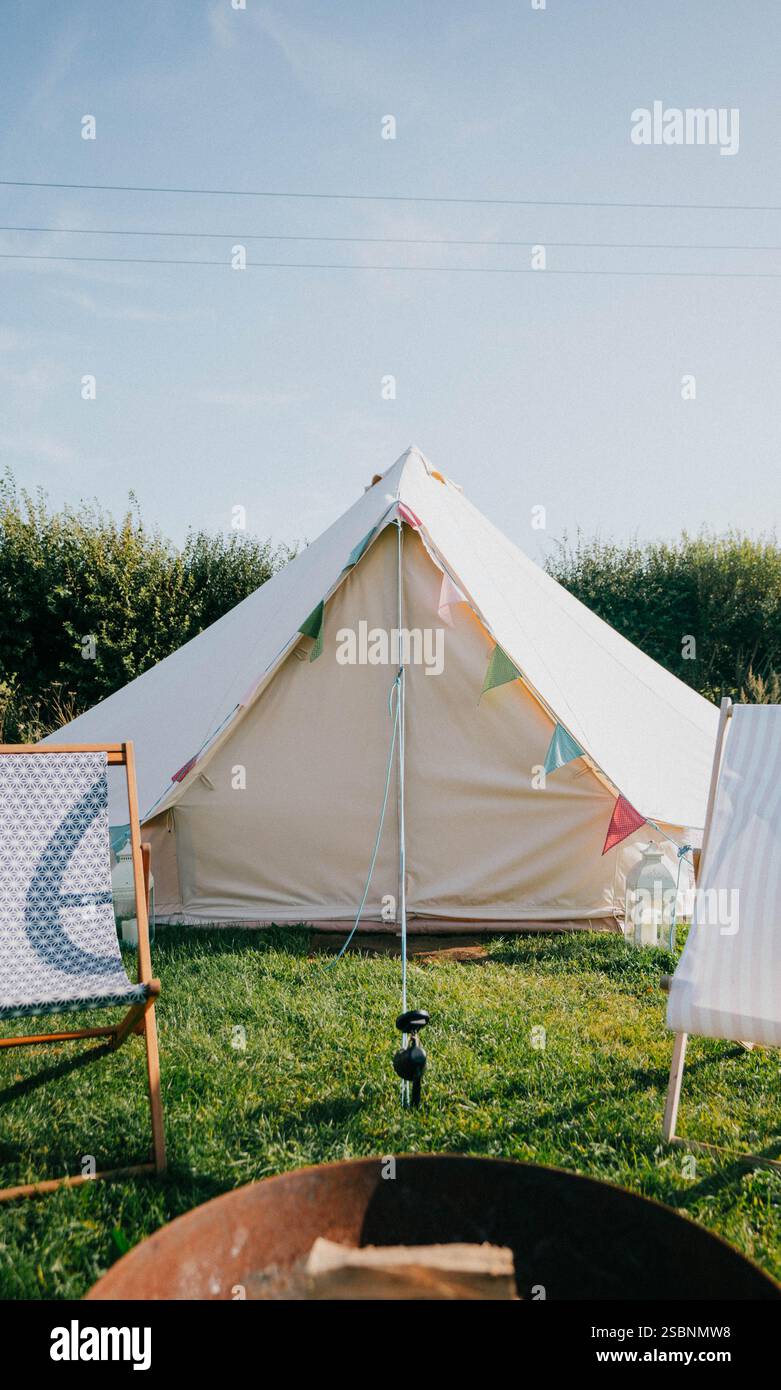 Ein weißes Zelt mit bunten Fahnen auf einem grasbewachsenen Feld. Ein Stuhl ist neben dem Zelt Stockfoto