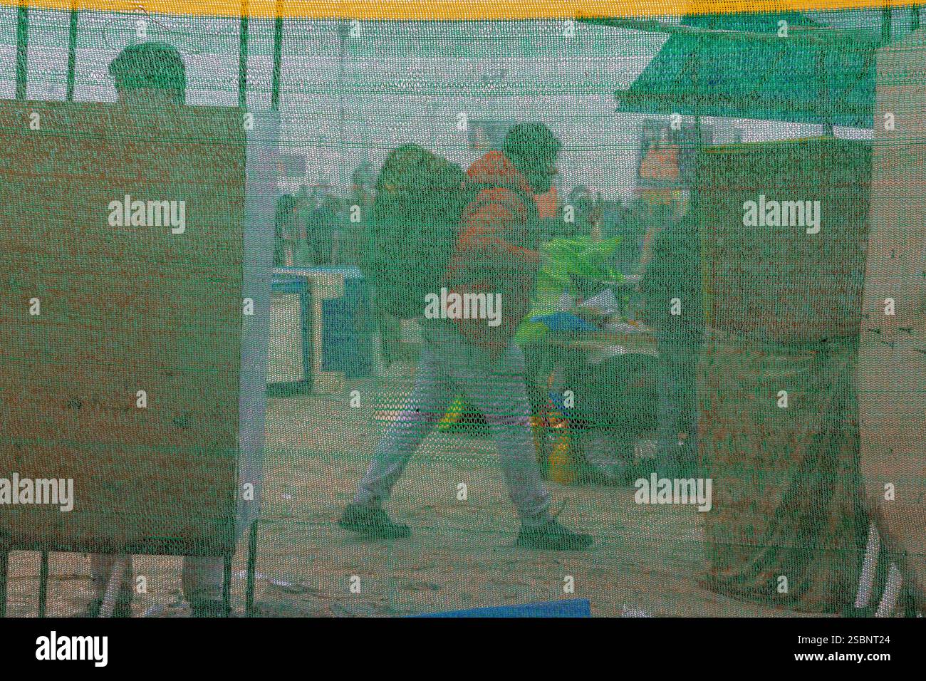 Ein Mann kommt vorbei, während ein anderer in einer halbtransparenten Toilette leicht sichtbar ist und einen Blick auf die Sanitäranlagen in Kumbh wirft. Stockfoto