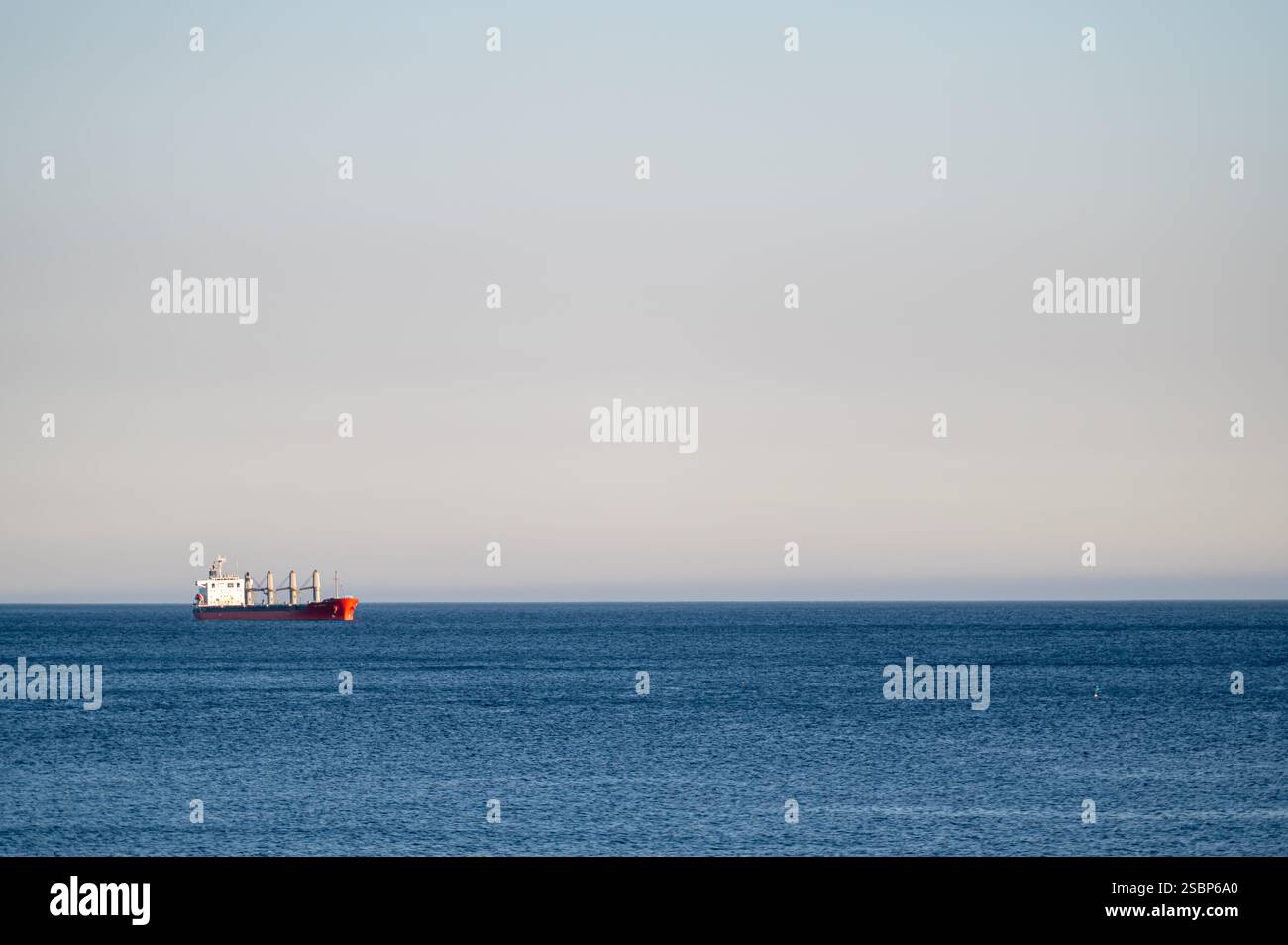 Ein Frachtschiff bewegt sich an klaren Tagen stetig über ein ruhiges Meer. Stockfoto
