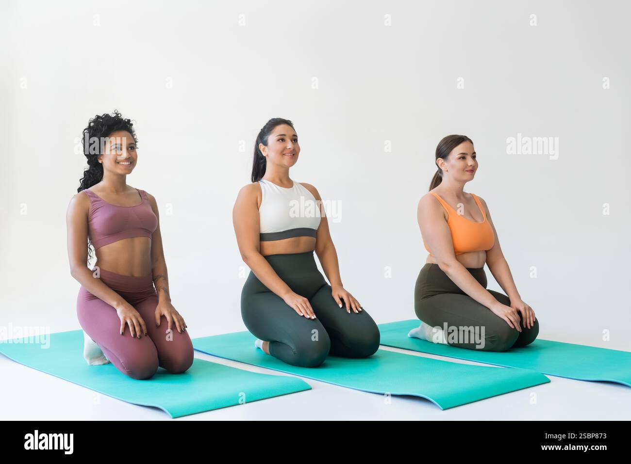 Drei starke Frauen nehmen in einem geräumigen Studio an einer Yoga-Session auf lebhaften Matten Teil. Stockfoto