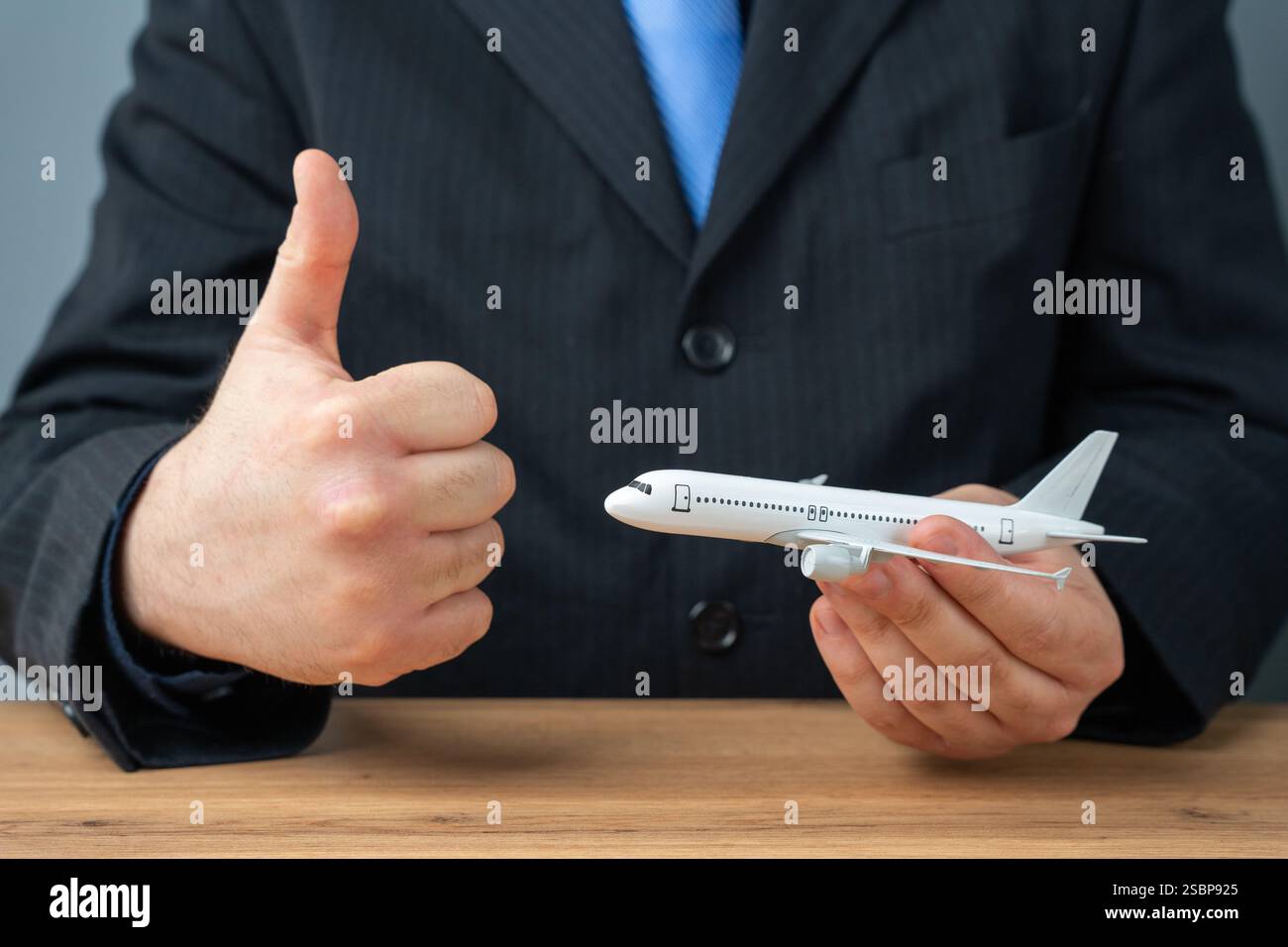 Ein Mann im Anzug hält ein Flugzeug und gibt eine Daumen-nach-oben-Geste. Fluggenehmigung. Tolle Angebote für Flugtickets. Treueprogramm und Bonus Air Stockfoto