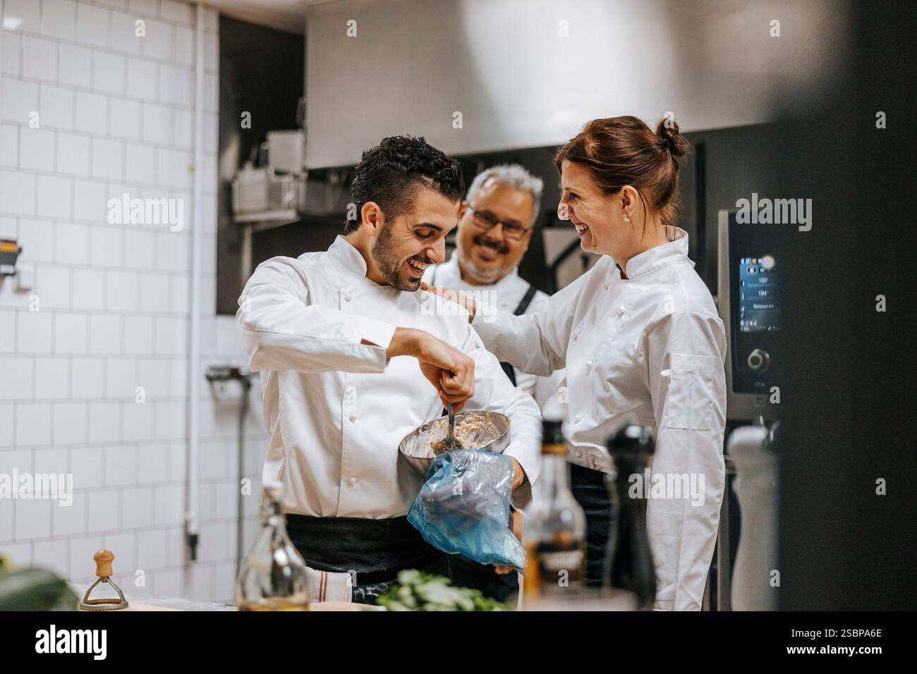 Glückliche Küchenchefin mit der Hand auf der Schulter eines männlichen Kollegen, der im Restaurant Teig in die Peitschentasche gelegt hat Stockfoto