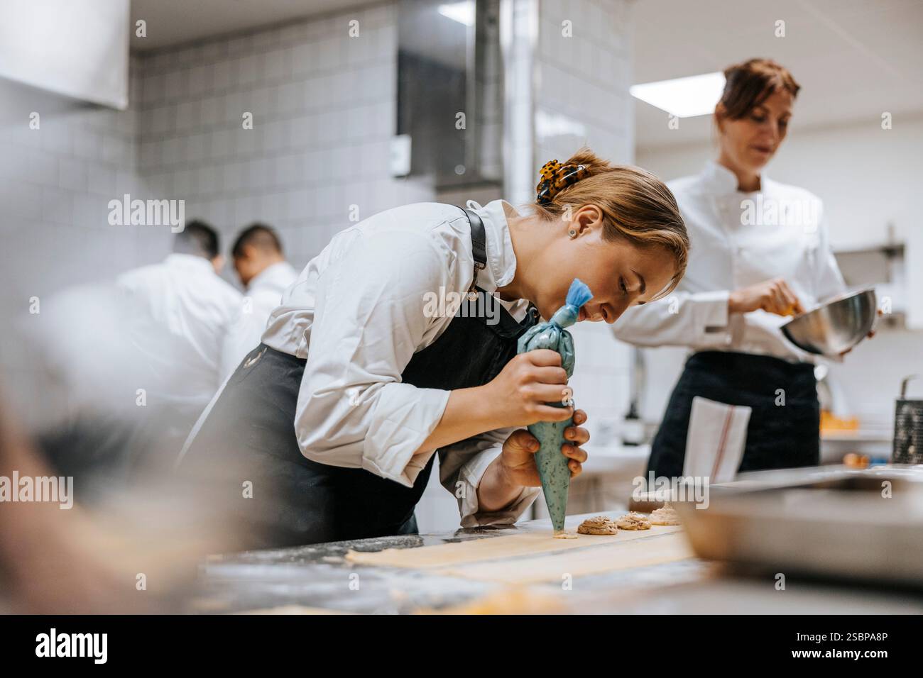 Junge Küchenchefin, die in der Restaurantküche Teig auf Teigblatt putzt Stockfoto